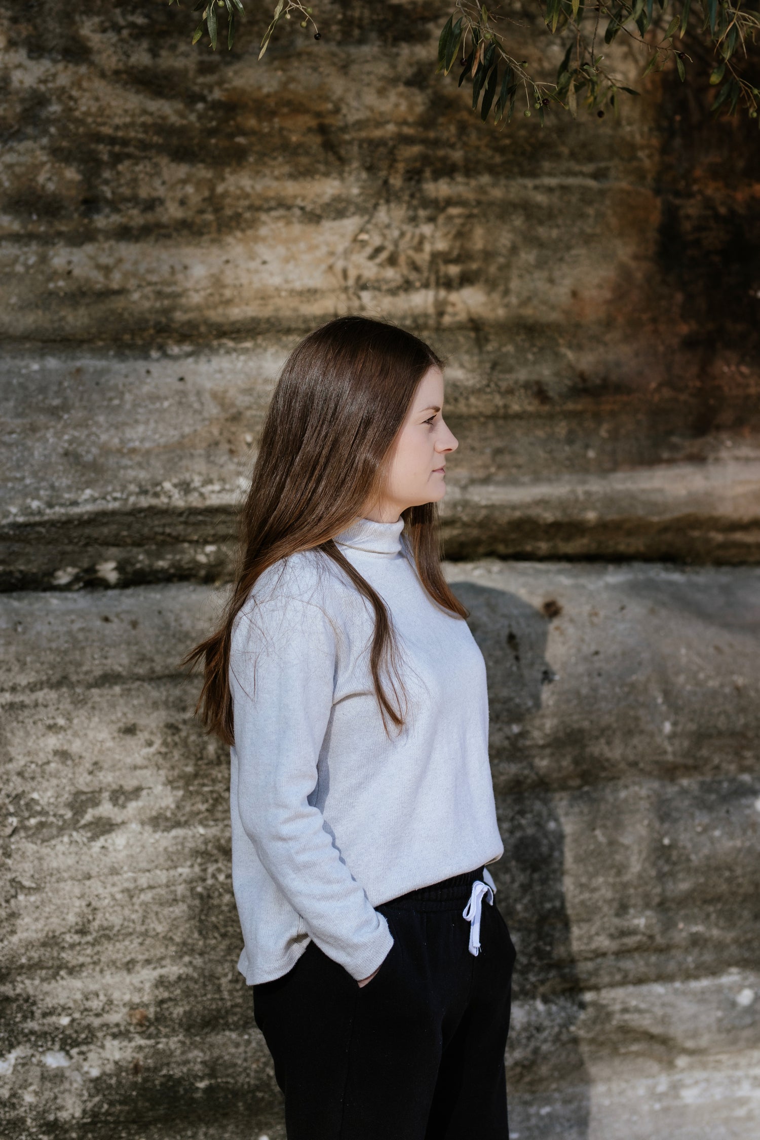 Short, petite woman standing side on, wearing a turtleneck knit jumper/sweater.