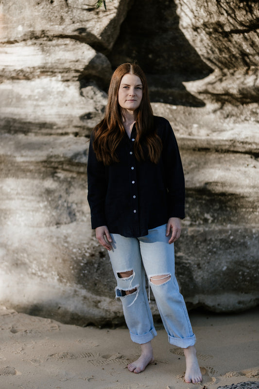 A short, petite woman standing front on in a linen shirt and jeans.