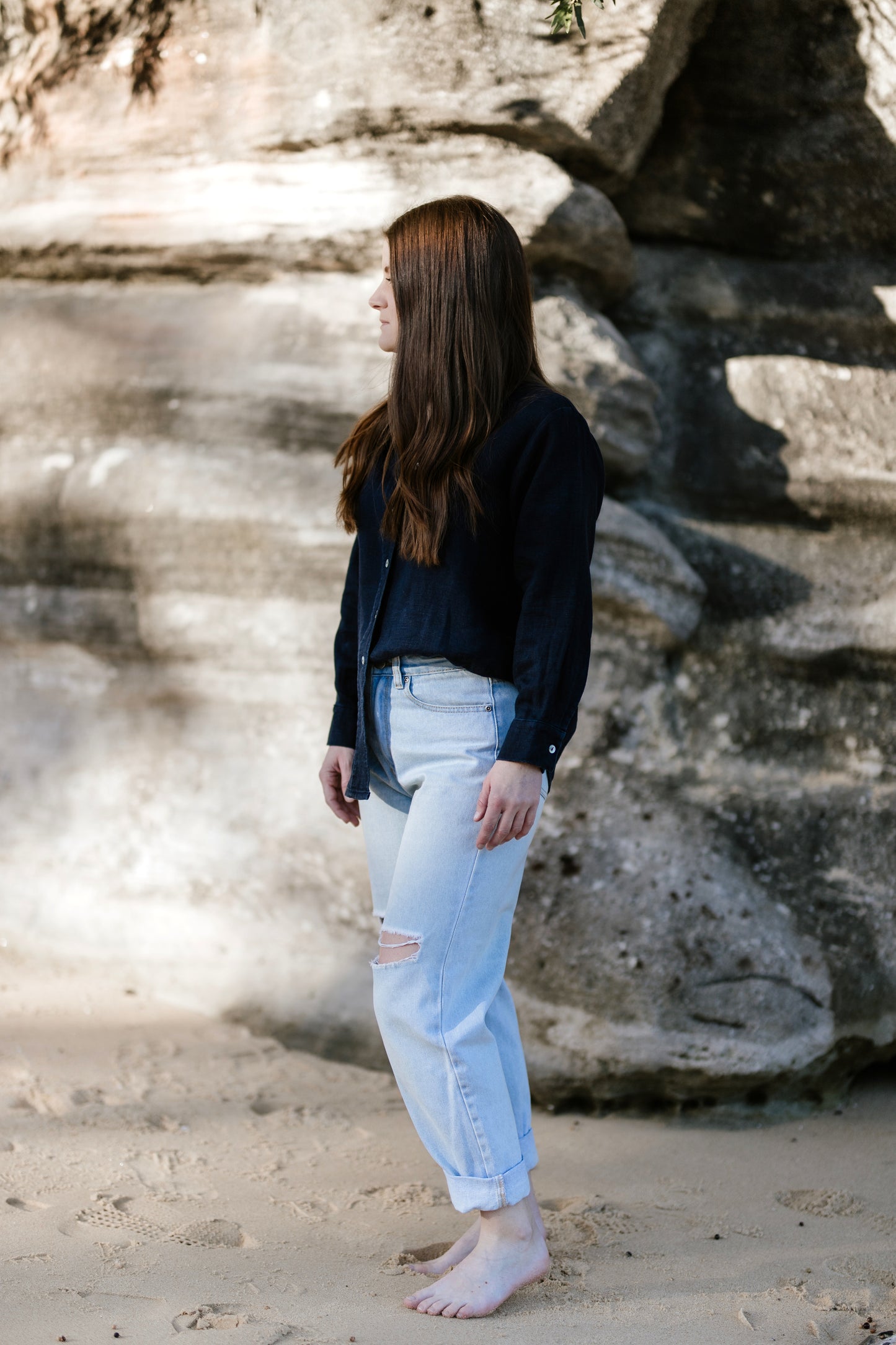 A short, petite woman standing side on in a linen shirt and jeans.