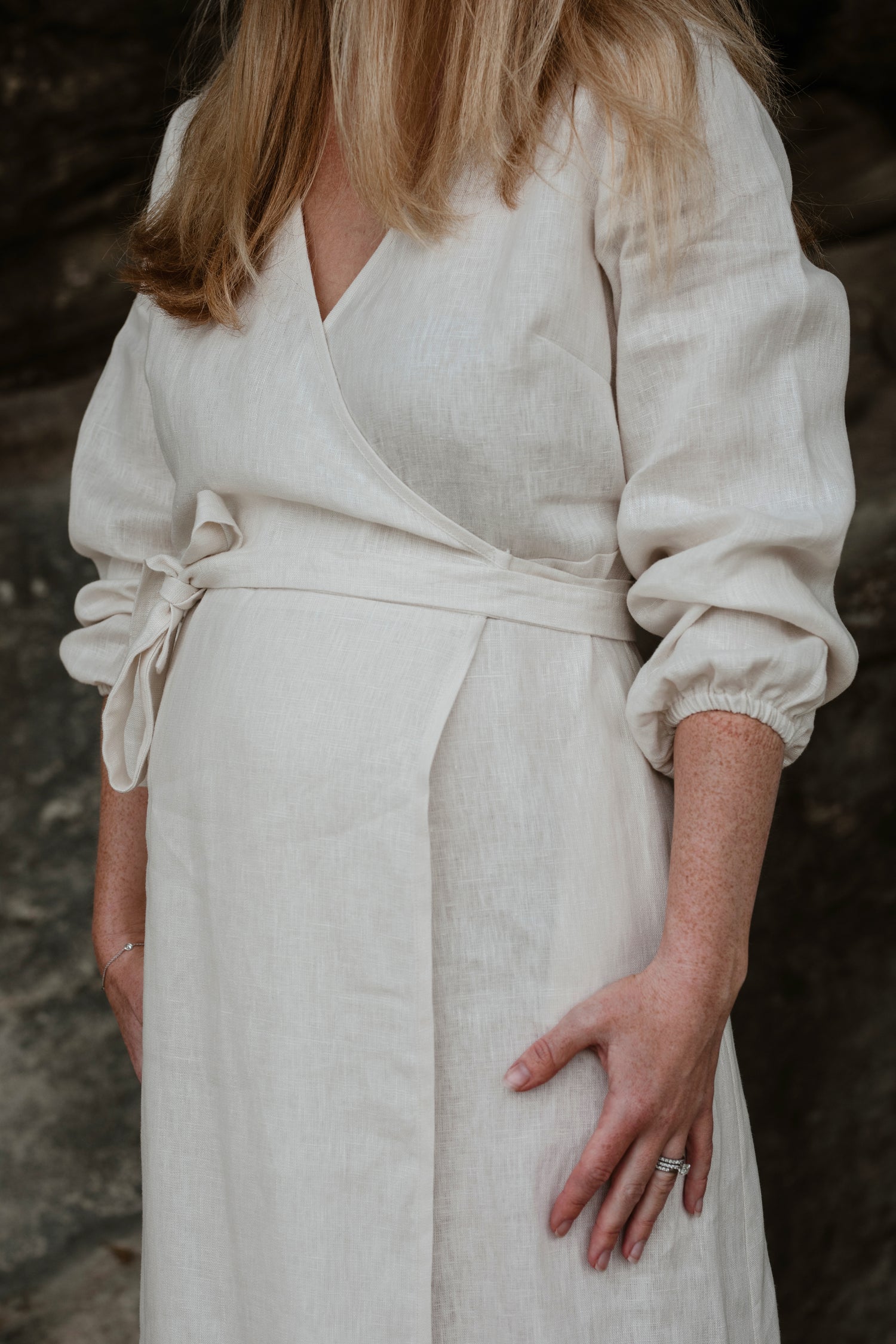A detailed close up of a short woman in a linen, off white wrap dress.