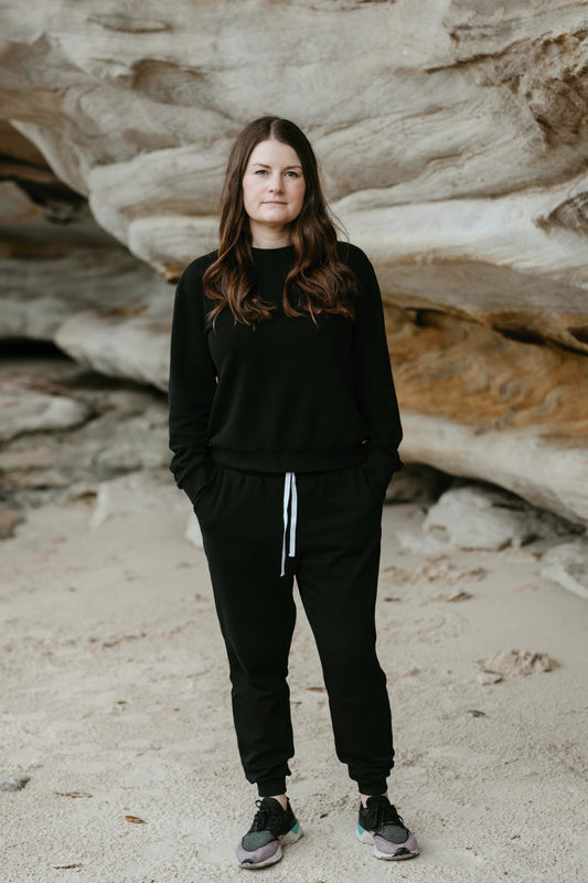 A petite woman standing front on, wearing a black tracksuit.